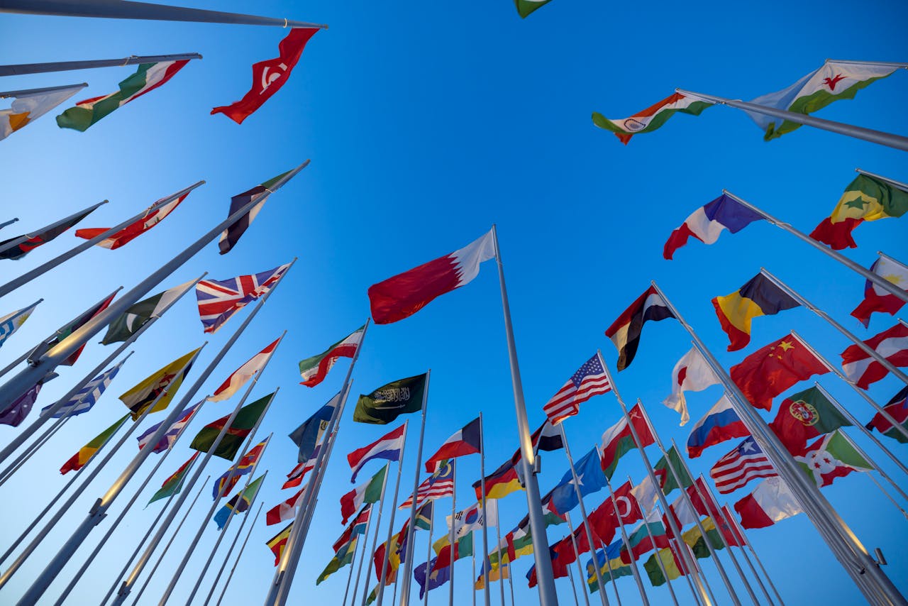 gallery-2 International flags waving against a clear blue sky in Doha, Qatar, symbolizing unity and diversity.