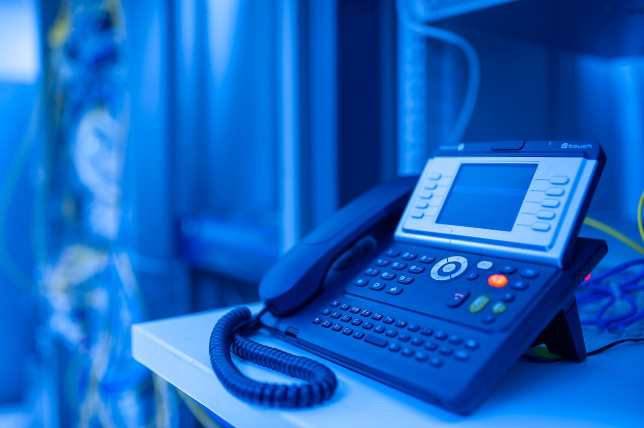 services-03 Close-up of a modern office phone in blue lighting. Ideal for tech and business themes.